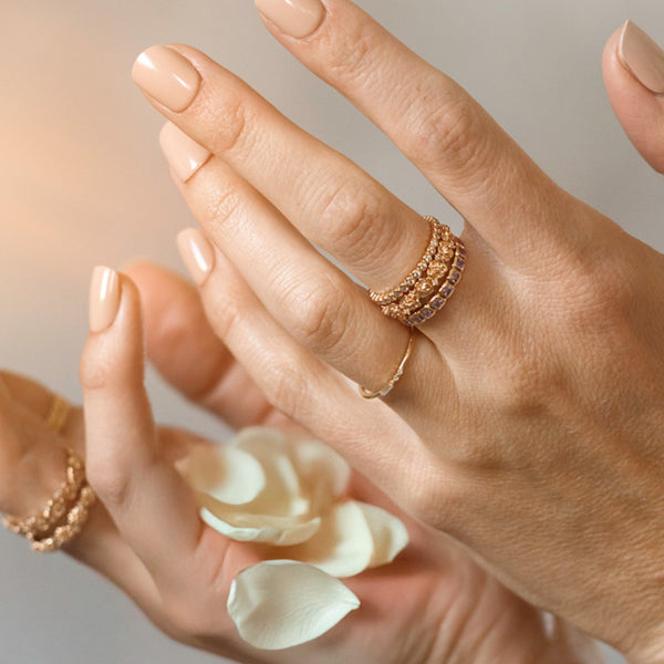 Hands throwing white flower petals, wearing stacked gold rings in various styles.