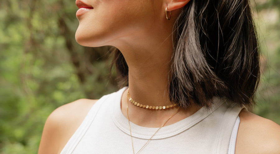 A woman in a white high neck tank top wearing multiple layered gold necklaces.
