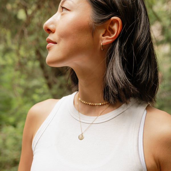 A woman in a white high neck tank top wearing multiple layered gold necklaces.
