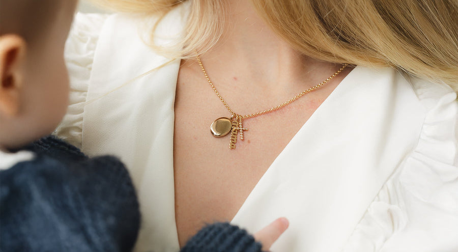A woman holding her child, wearing a gold charm necklace.