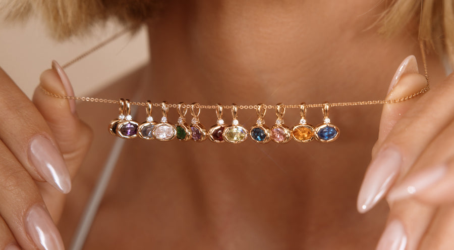 A person holding a delicate gold chain necklace with multiple oval gemstone charms in different colors.