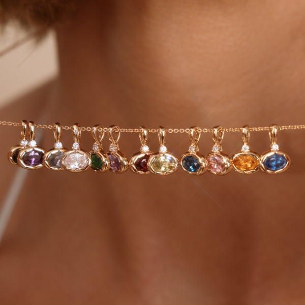 A person holding a delicate gold chain necklace with multiple oval gemstone charms in different colors.