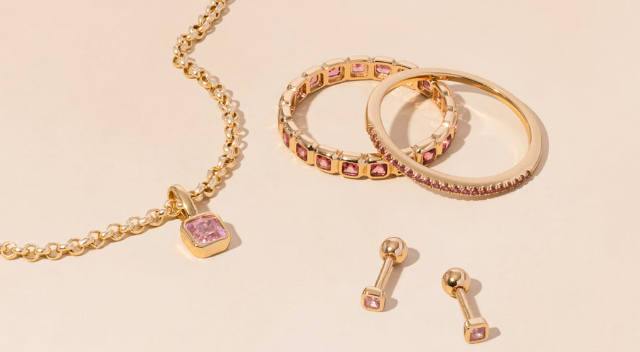 A gold necklace, rings, and earrings all adorned with light pink gemstones.