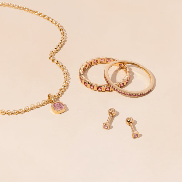 A gold necklace, rings, and earrings all adorned with light pink gemstones.