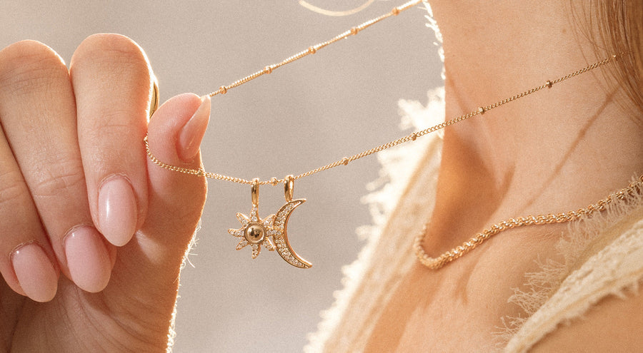 A woman wearing a delicate gold pendant chain with a sun and moon charm.