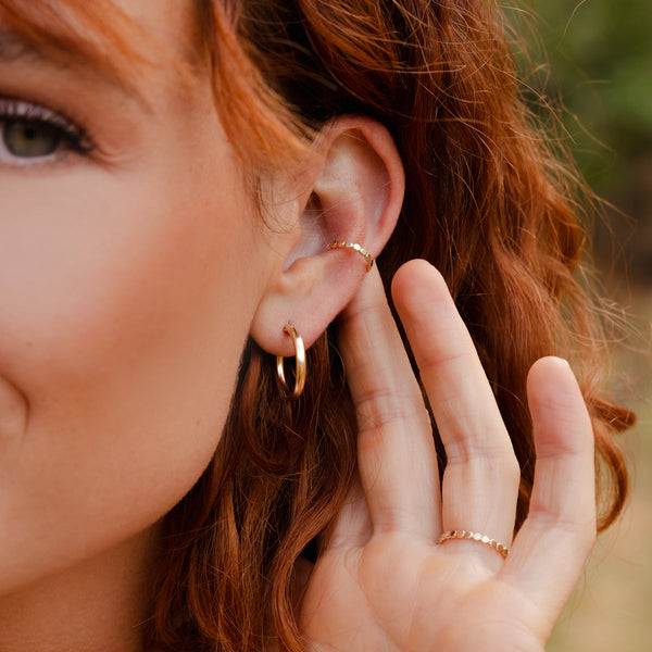 A model's ear wearing a polished gold hoop and a gold ear cuff.