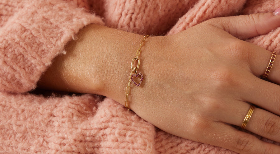 A person wearing a gold chain charm bracelet with multiple charms.