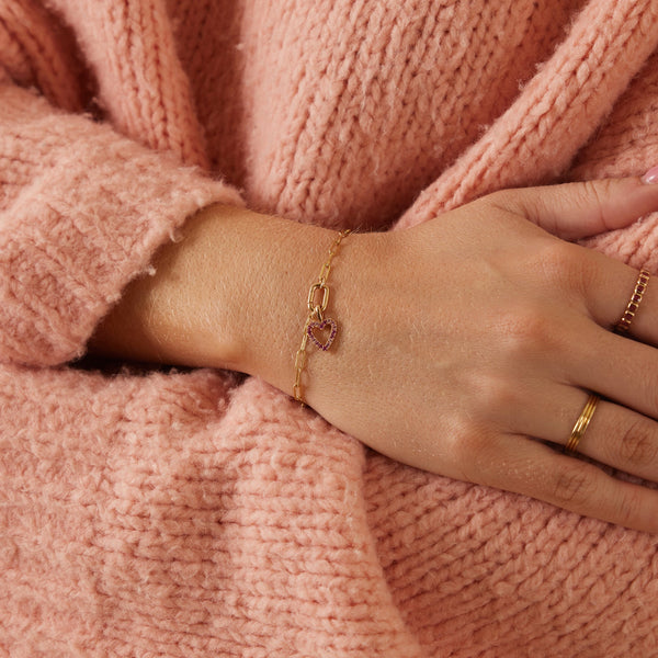 A person wearing a gold chain charm bracelet with multiple charms.