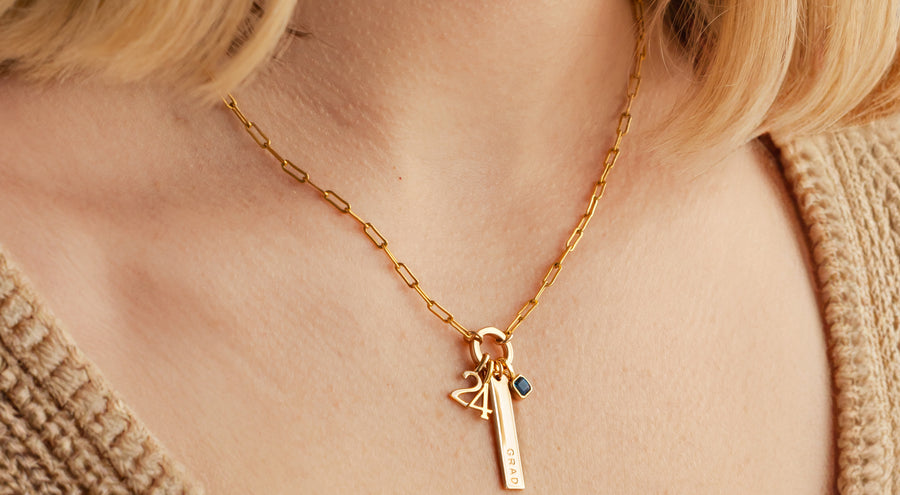 A model wearing a gold chain charm necklace with a ring in the center, holding multiple gold charms.