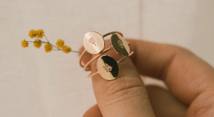 A person's hand holding three gold oval rings with engraving.