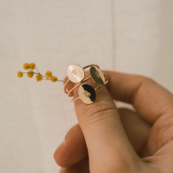 A person's hand holding three gold oval rings with engraving.