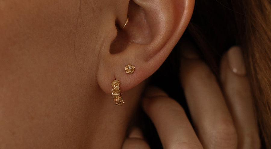 Close-up of a person wearing gold hoop earrings made up of a textured floral design and a matching stud earring with a singular floral motif.