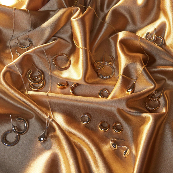 Multiple pieces of gold jewelry laying on a light pink satin background.