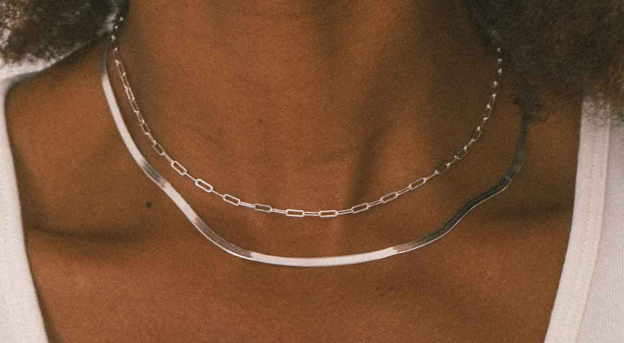 A person wearing two layered silver chain necklaces.