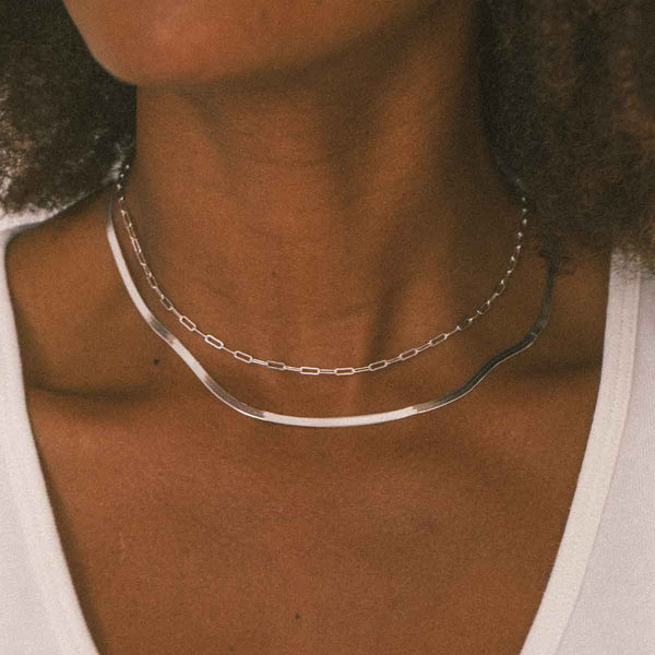A person wearing two layered silver chain necklaces.