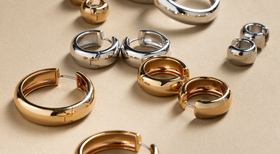 Multiple sizes of gold and silver chunky hoop earrings, laying scattered on a white surface with shadows.