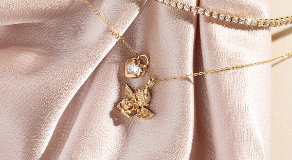 A delicate gold pendant chain necklace with a gold cupid charm and a gold heart charm.