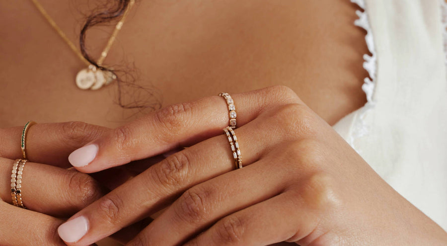 Close-up of a woman's hand wearing multiple gold rings with different styles of clear stones.