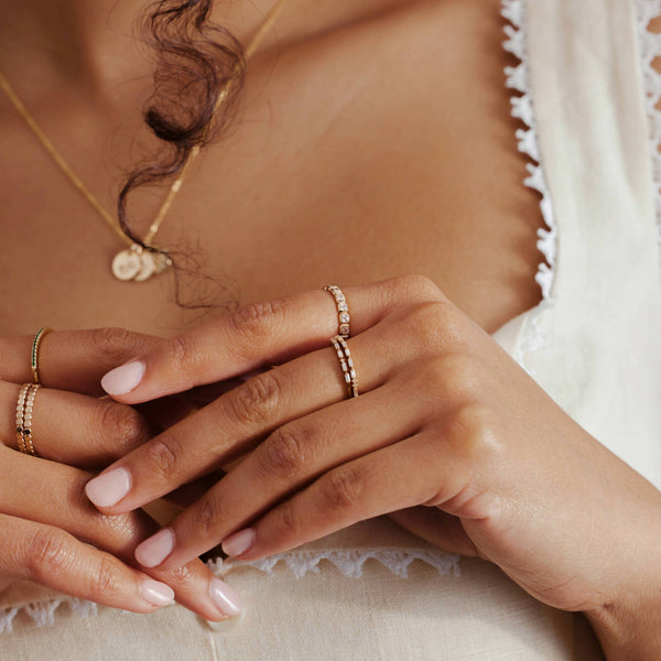 Close-up of a woman's hand wearing multiple gold rings with different styles of clear stones.