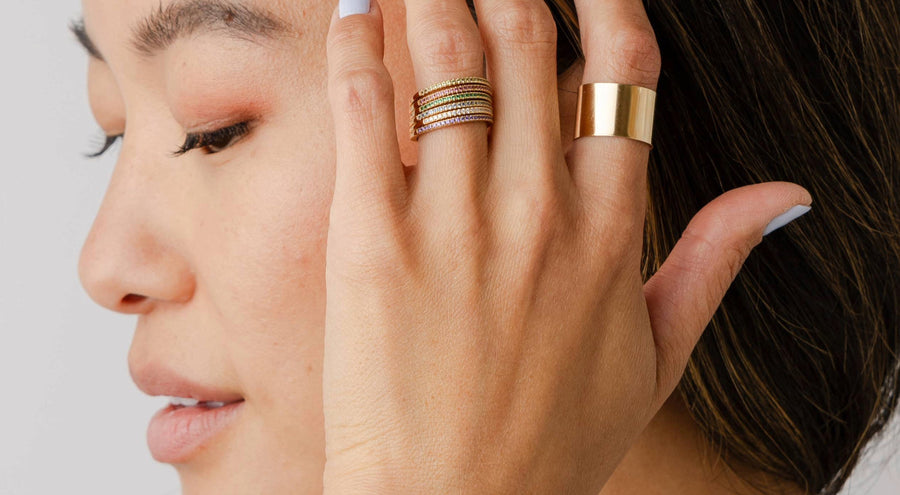 A person holding their hand to their face wearing multiple stacked gold rings with different colored gemstones.