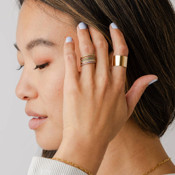 A person holding their hand to their face wearing multiple stacked gold rings with different colored gemstones.