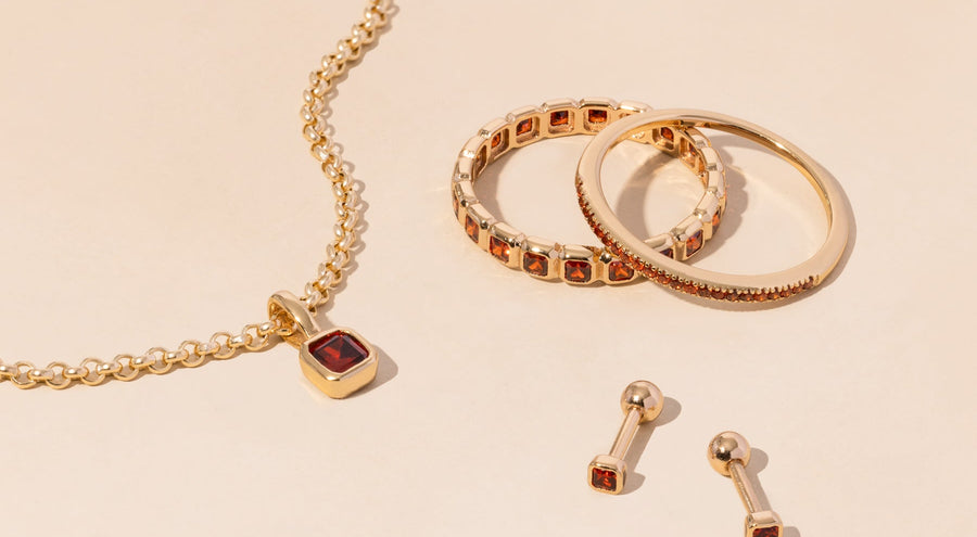 A gold necklace, rings, and earrings all adorned with red gemstones.