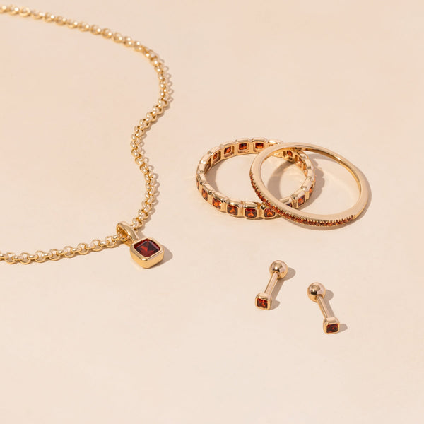 A gold necklace, rings, and earrings all adorned with red gemstones.