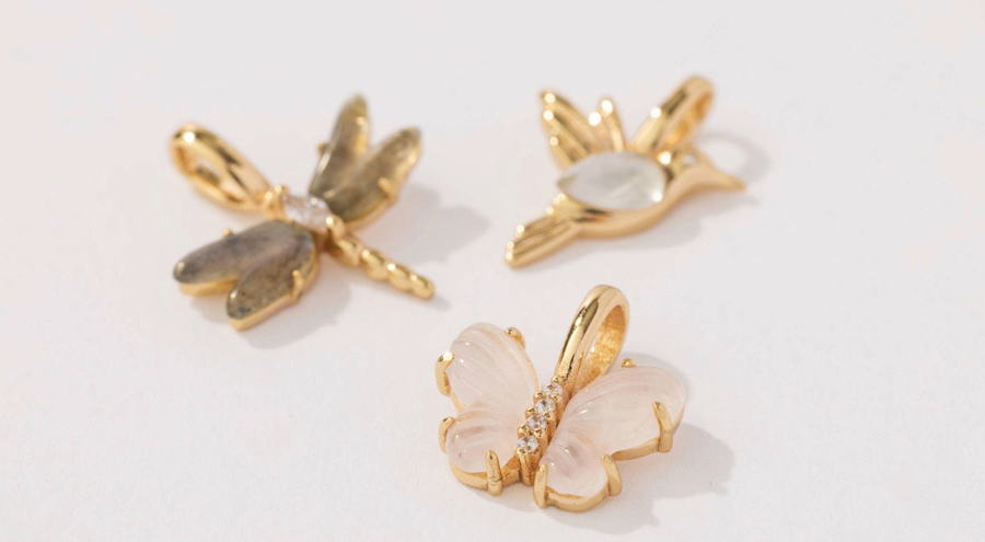 Three gold charms: a dragonfly, butterfly, and hummingbird. Each charm is inlayed with different colors of natural gemstones.