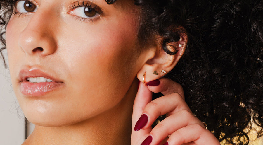 A model holding her ear wearing multiple gold earrings.