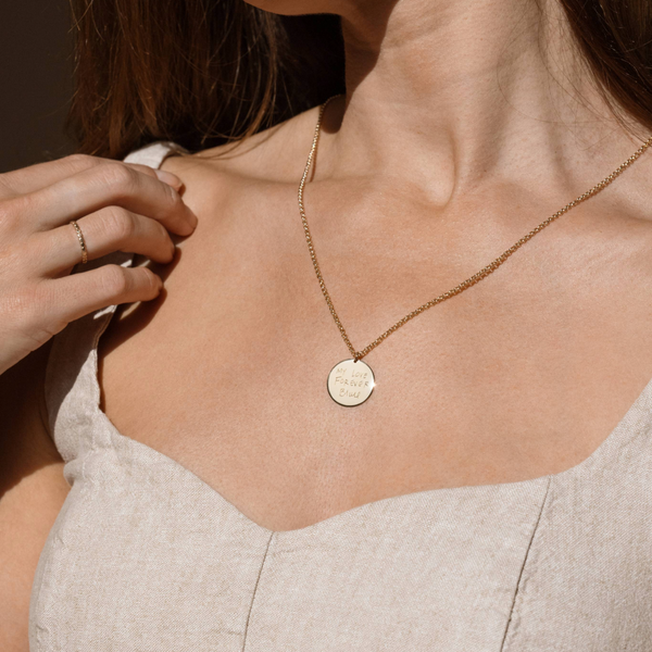 A personalized round disc necklace engraved with custom text, part of Made By Mary's engraving collection.