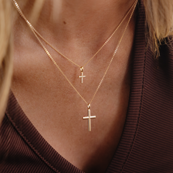 A model wearing two layered gold cross pendant necklaces.