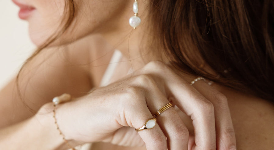 A woman's hand resting on her shoulder, wearing multiple pieces of gold and pearl jewelry.