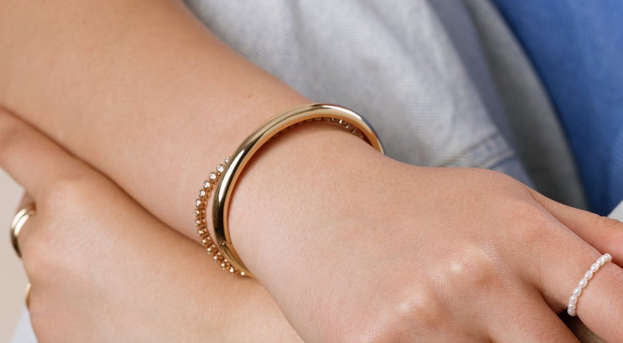 A model wearing a gold polished cuff bracelet and a gold tennis bracelet, paired with multiple gold rings.
