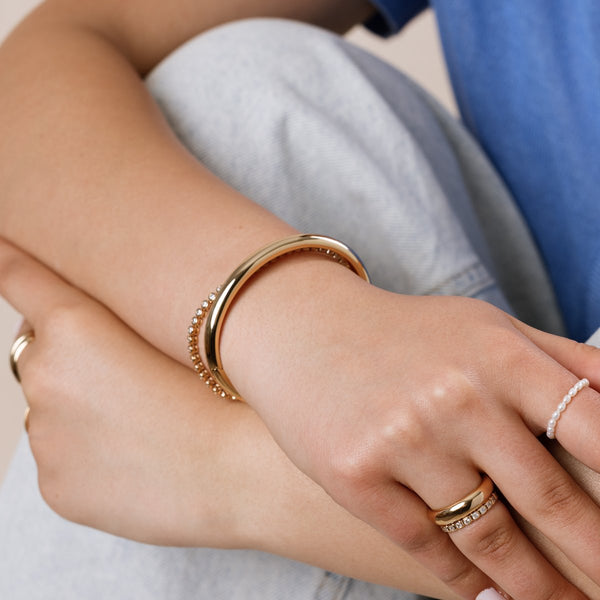 A model wearing a gold polished cuff bracelet and a gold tennis bracelet, paired with multiple gold rings.