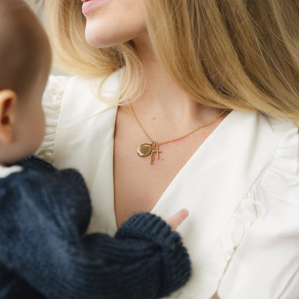 Close-up of a woman holding her child, wearing a gold chain necklace with multiple charms.