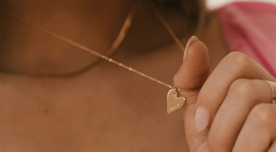 A person wearing a gold pendant necklace with a gold heart charm.