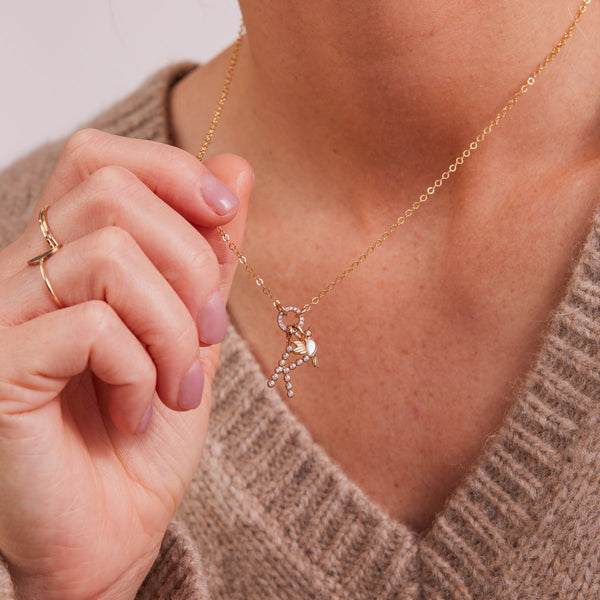 A person wearing a gold pendant chain necklace with layered charms.