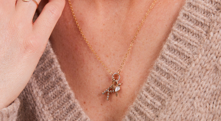 A woman in a beige v-neck knit sweater wearing a gold pendant necklace with multiple charms.