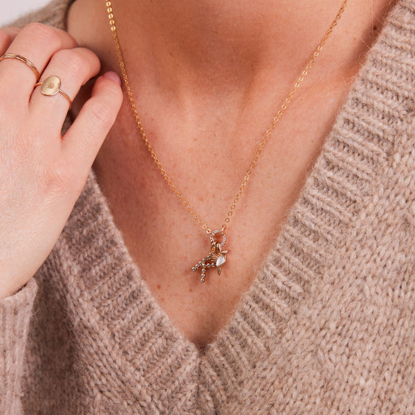 A woman in a beige v-neck knit sweater wearing a gold pendant necklace with multiple charms.
