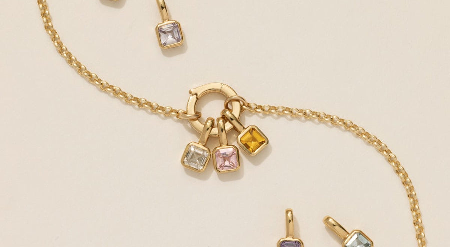 A gold chain charm necklace with multiple square gemstones with different colored stones.