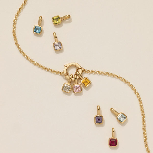 A gold chain charm necklace with multiple square gemstones with different colored stones.