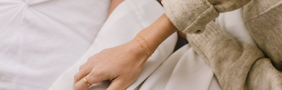 A woman's wrist wearing two delicate gold bracelets with small round stationary beads.