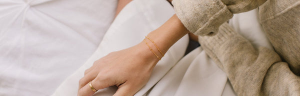 A woman's wrist wearing two delicate gold bracelets with small round stationary beads.