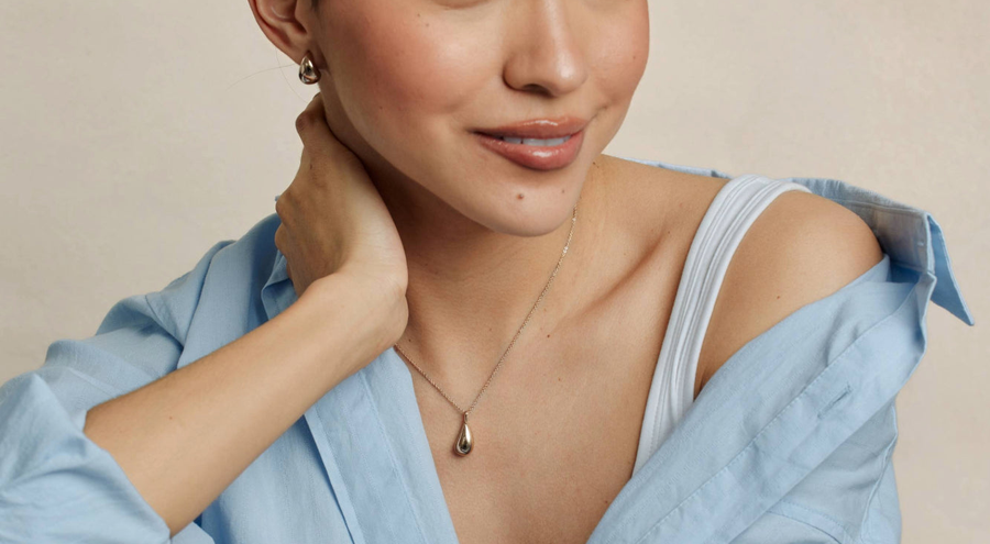 A person wearing a delicate silver pendant necklace with a polished teardrop charm and matching earrings.