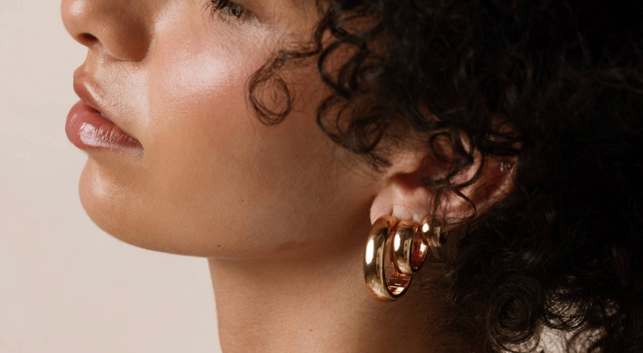 The profile of a woman's head wearing multiple gold hoop earrings.