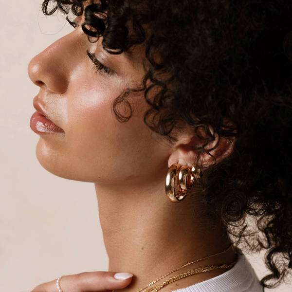 The profile of a woman's head wearing multiple gold hoop earrings.