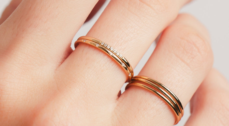 A hand wearing five gold stacked rings, two with small diamonds in different shapes.