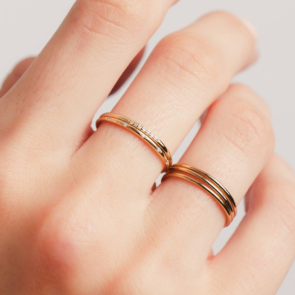 A hand wearing five gold stacked rings, two with small diamonds in different shapes.