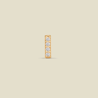A yellow-gold bar earring, set vertically with four round-cut diamonds adorning the front, set against a solid beige background