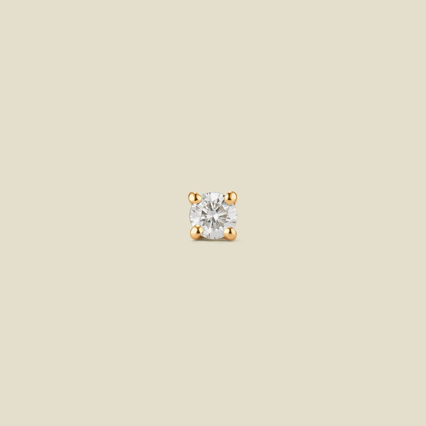 A yellow gold, prong-set single diamond stud earring on a beige background